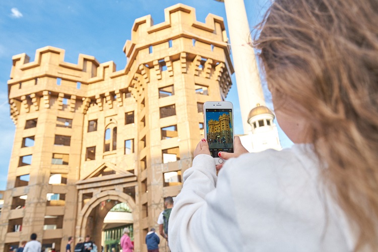 Young girl taking a picture of a huge castle made of cardboard