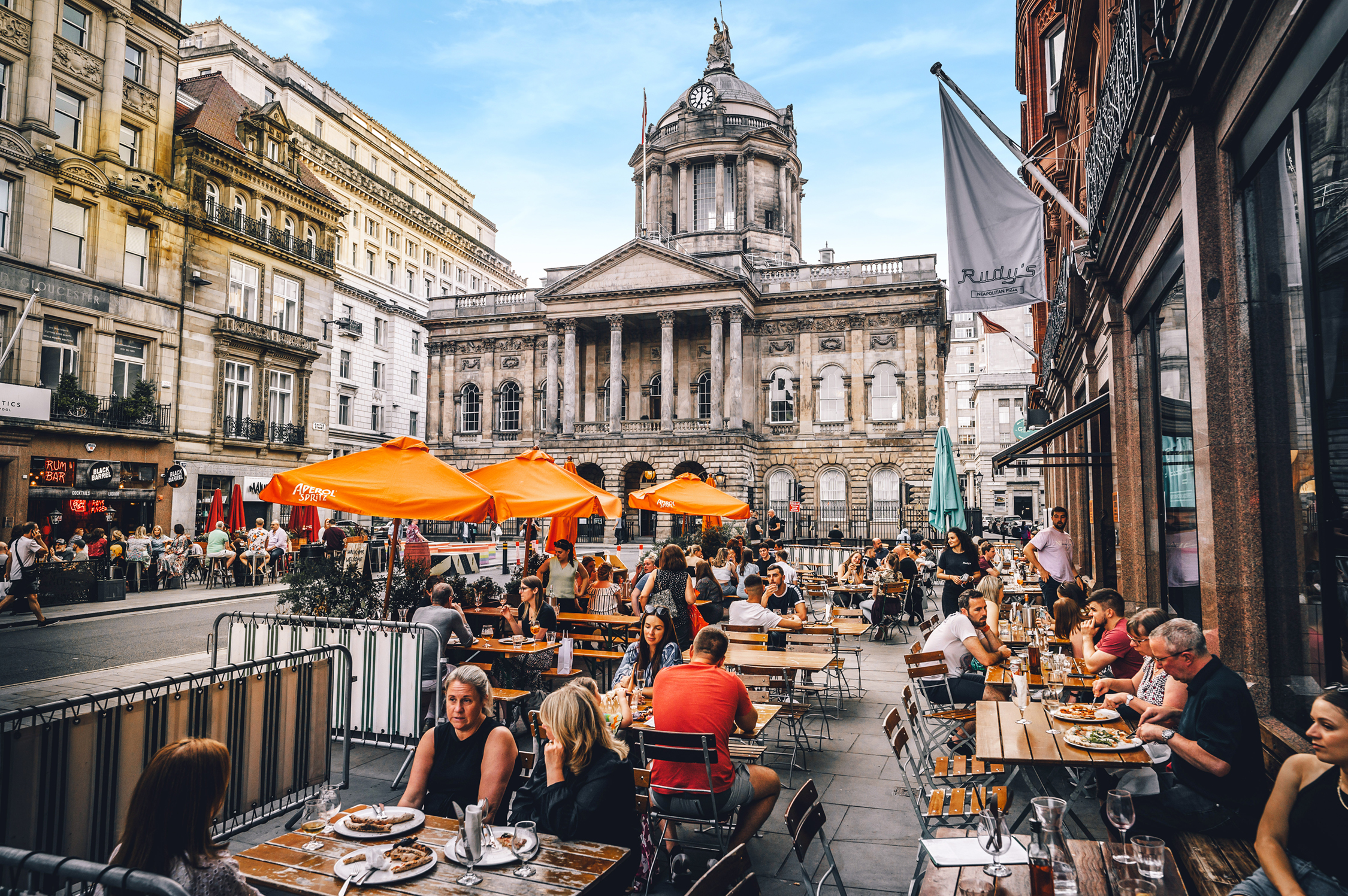 People sitting outside restaurants on Castle St, with the Town Hall in the background