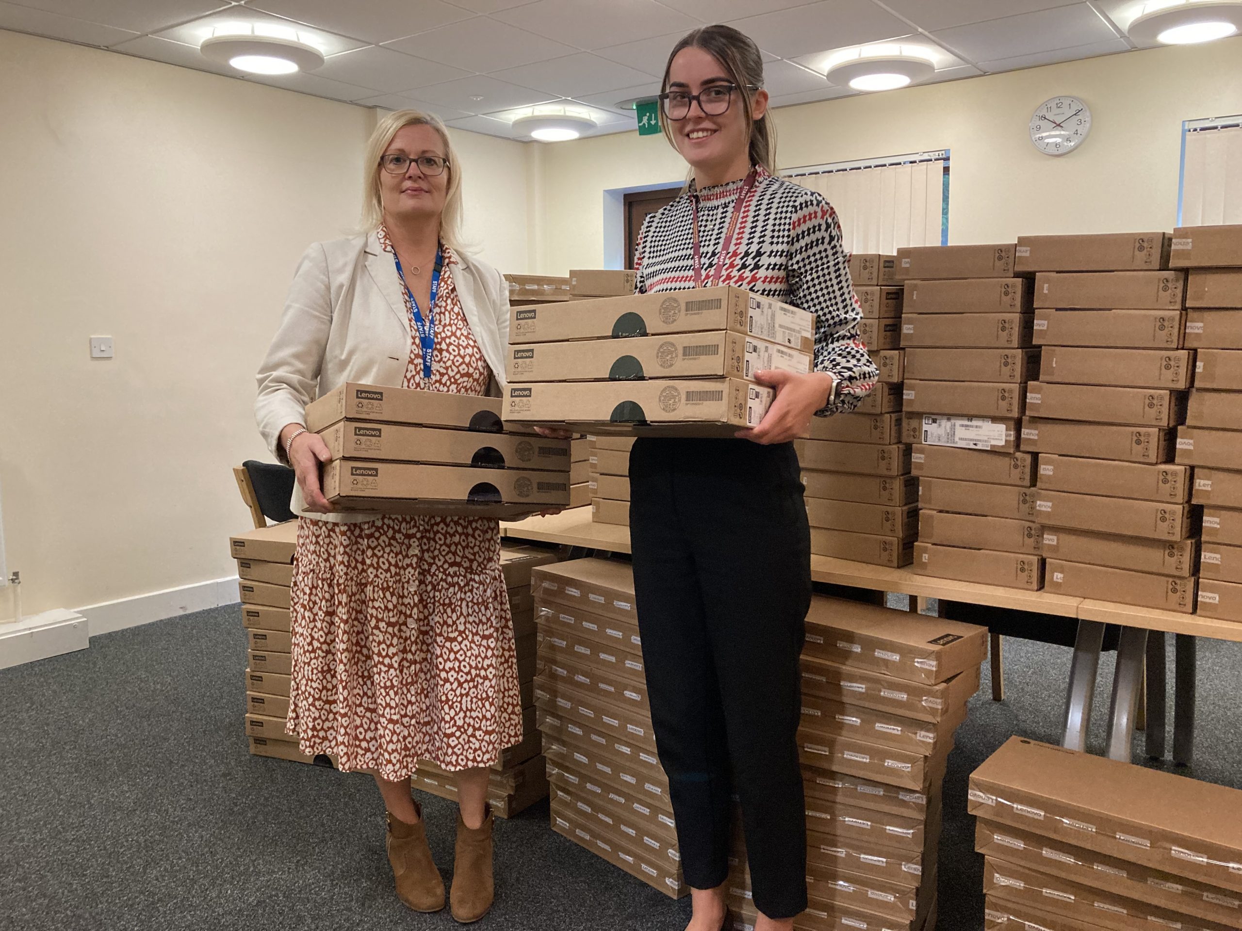 Two women holding boxes in front of a pile of boxes