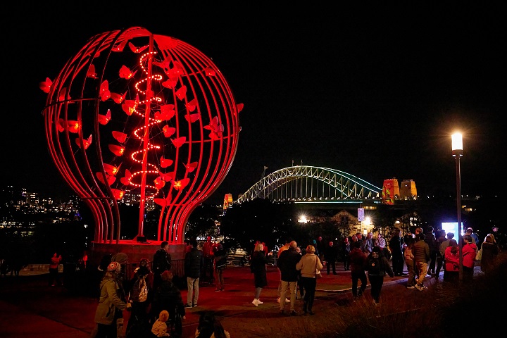 Image of a huge art installation which is lightbulb shaped with moths flying around it, bathed in red light