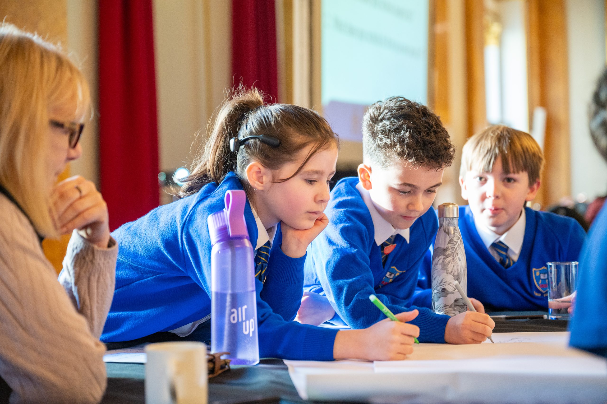 Three school children in blue school uniforms and an adult sitting at a table