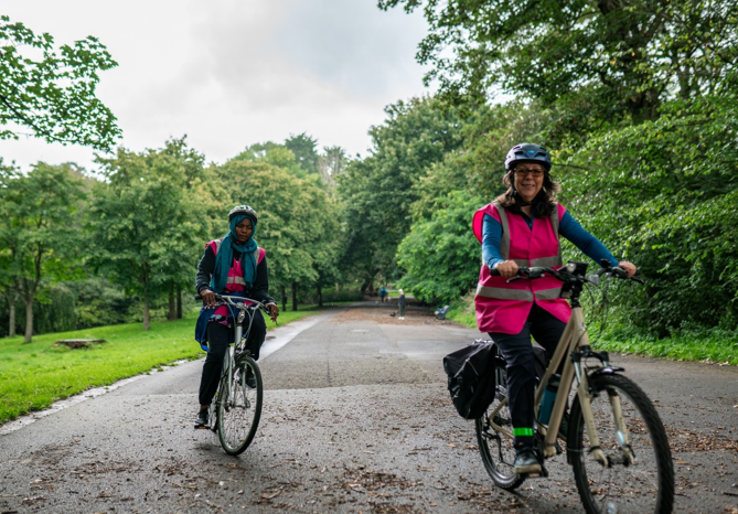 Two women riding on a bike through a park