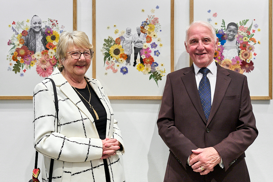 A woman and man standing in an art gallery in front of a picture of them