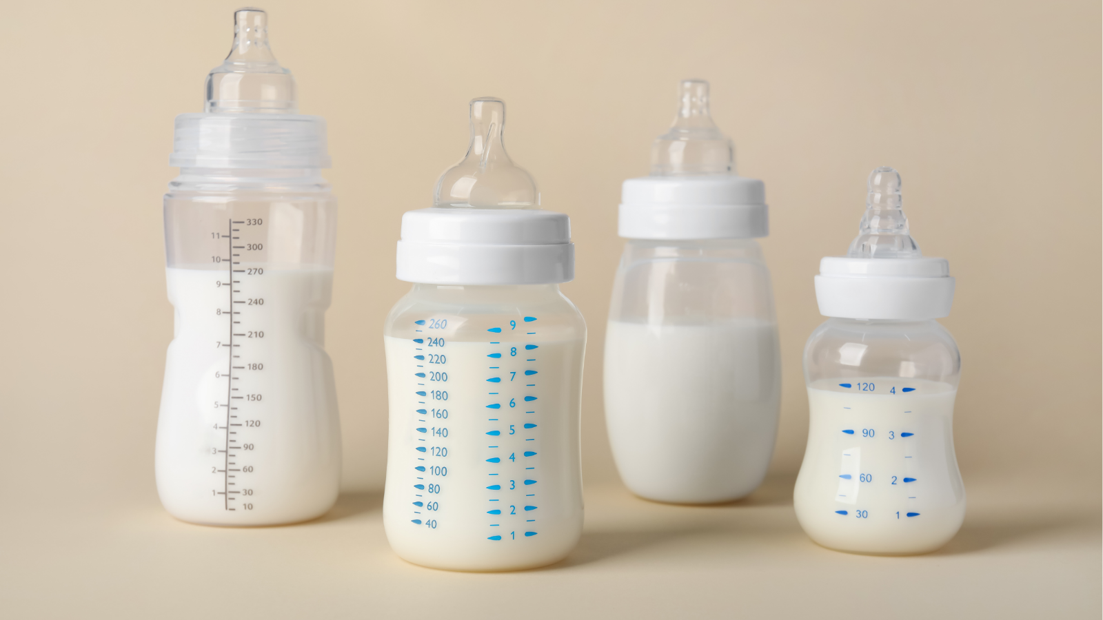 "Four baby bottles filled with milk, varying in size and measurement markings, displayed on a neutral beige background."