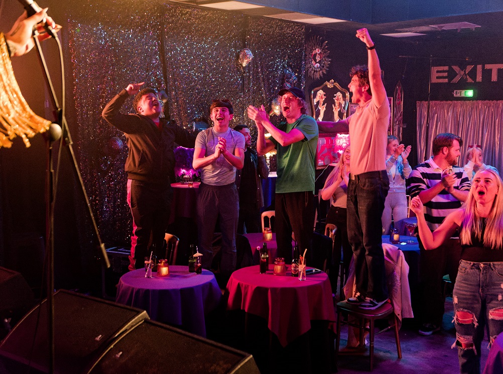 Young men in a pub setting cheering.