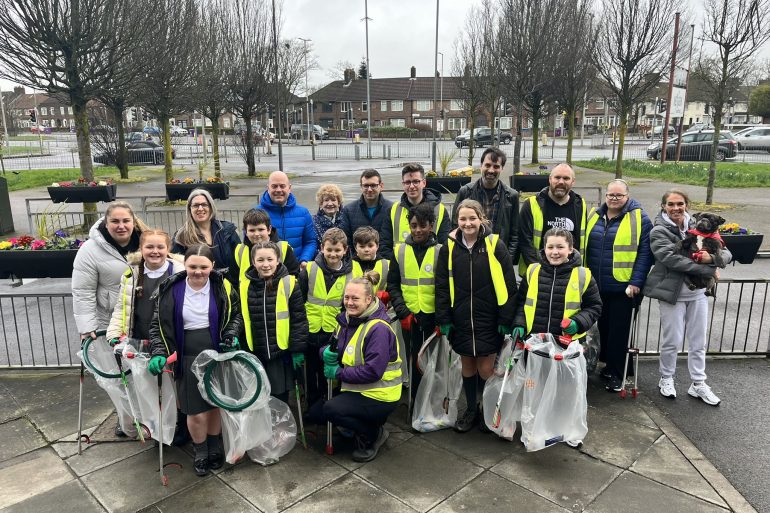 Litter picking volunteers stood in high-vis vests holding bags of litter.