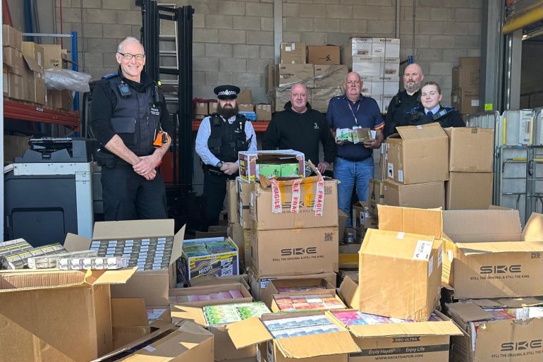 Staff from Merseyside Police and Trading Standards stood behind boxes of seized vapes and cigarettes
