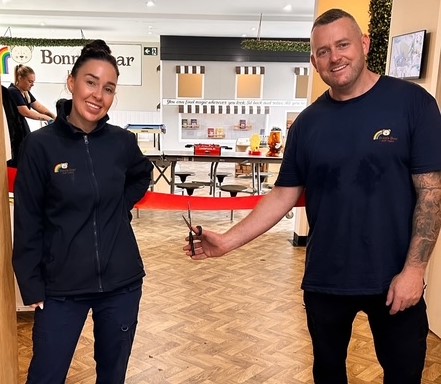 Two people cutting a red ribbon